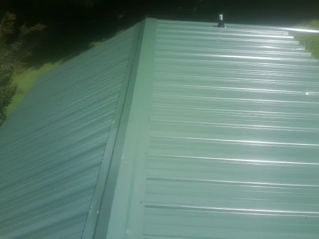 New green metal panels meeting at the ridge of a roof — Flat Roof Repair work by our crew in Duncansville
