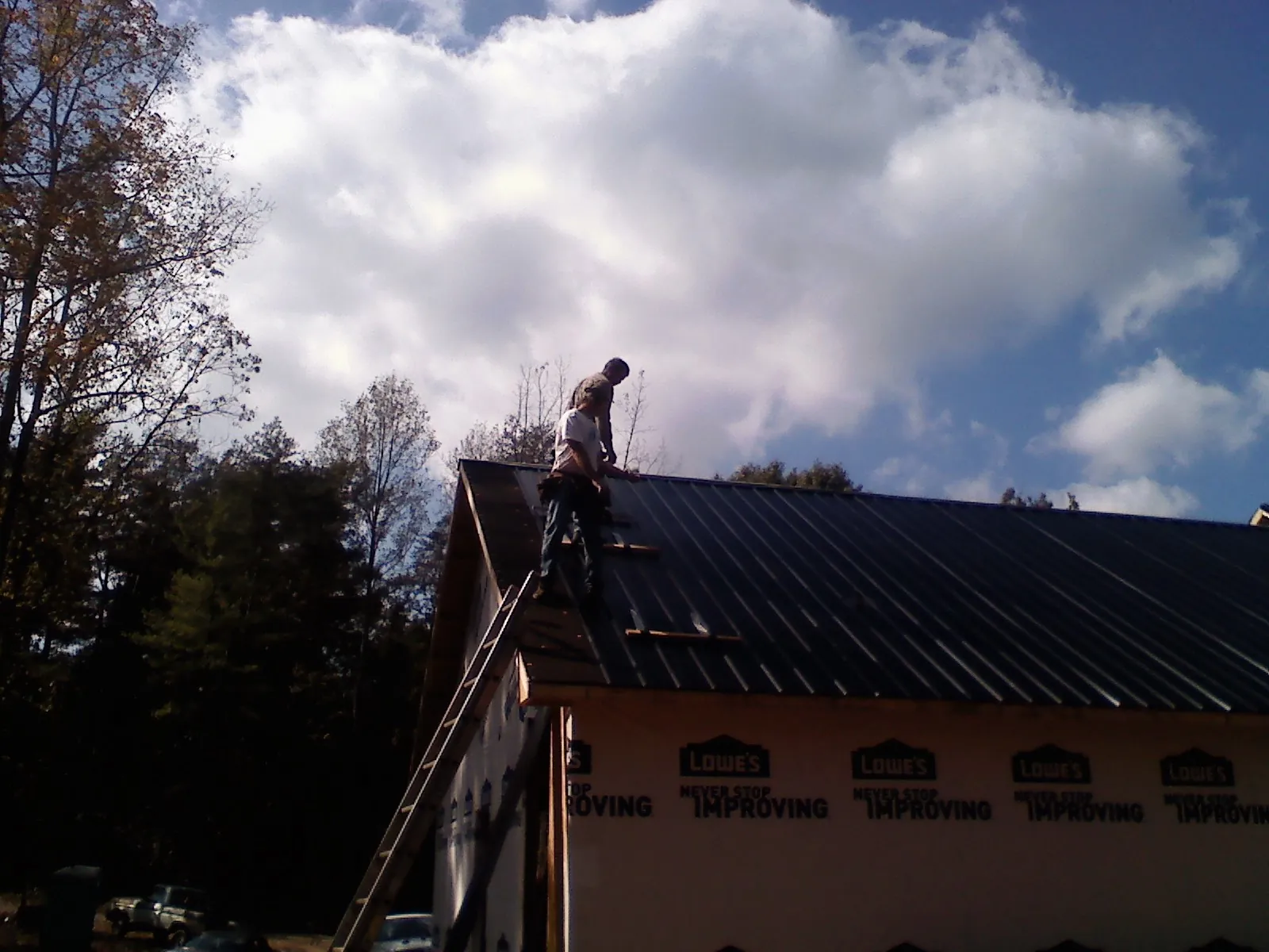 Roofer fastening dark metal panels high against a cloudy sky, from a Roof Inspection job in Duncansville