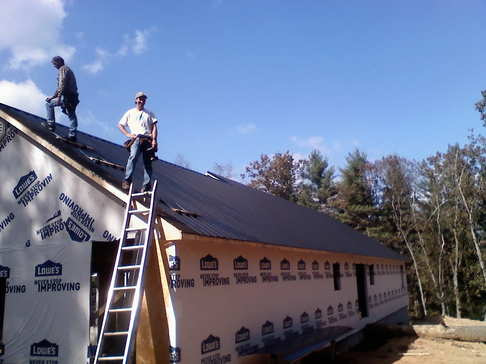 Two roofers standing on a long dark metal roof over a wrapped building in Duncansville