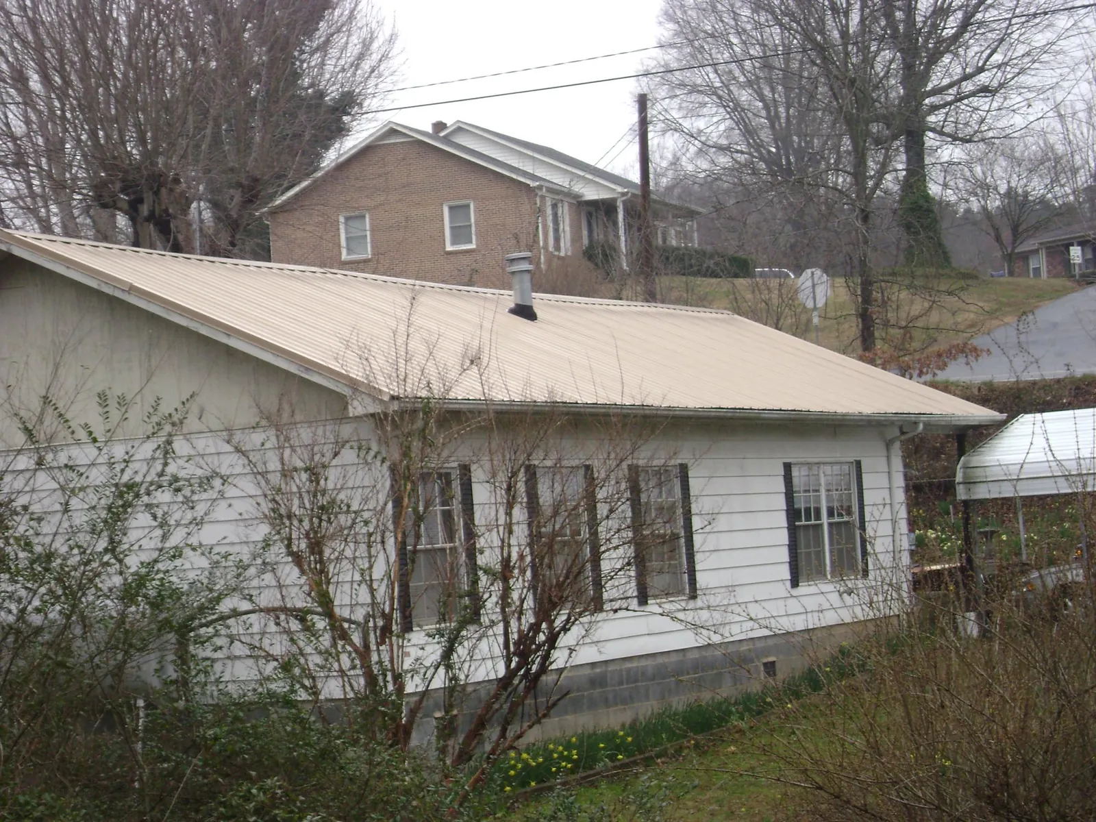 Tan metal roof on a white sided house set into a hillside — Commercial Roofing by Roofing Brothers in Duncansville